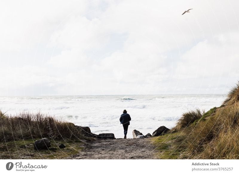 Unrecognizable male traveler walking towards sea man stormy foam cloudy beach tourist usa united states america ocean water wave weekend summer shore coast