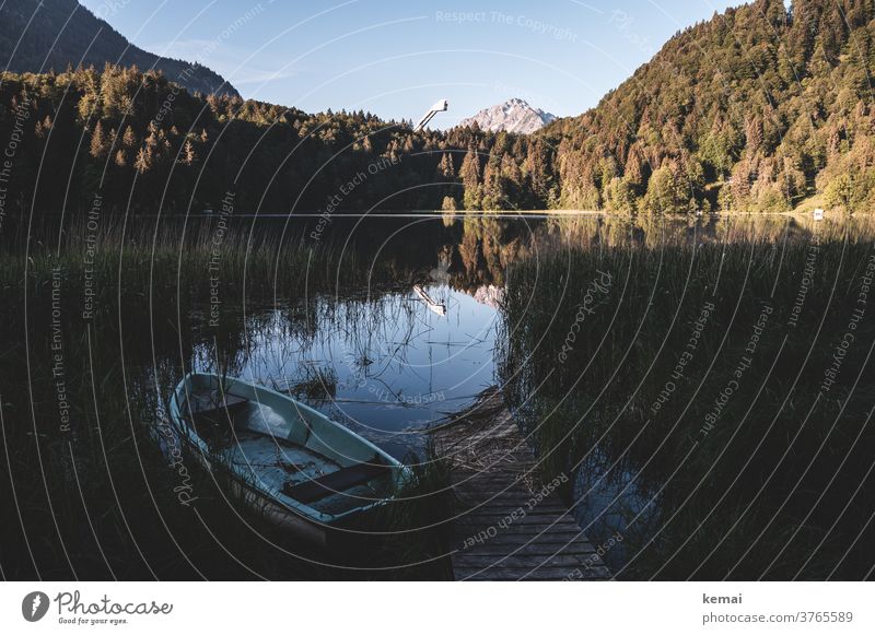 Boat and jetty on a lake Lake Water boat Idyll Footbridge Reflection Nature mountain Allgäu ski jumping hill Forest trees bank reed Rowboat