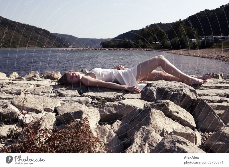 Backlit portrait of a young, barefoot woman on the banks of the Rhine, lying on a dam Woman Young woman Slim already athletic Blonde youthful 18-25 years