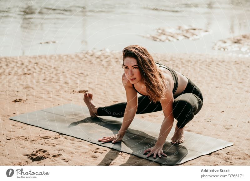 Peaceful woman doing yoga in Skandasana on river bank side lunge skandasana pose outstretch calm zen posture beach female mat balance summer healthy wellness