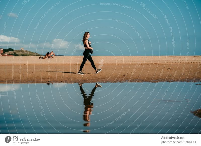 Woman with mat walking along beach yogi woman summer sportswear slim sunny yoga female water wellness harmony river riverside river bank shore activewear