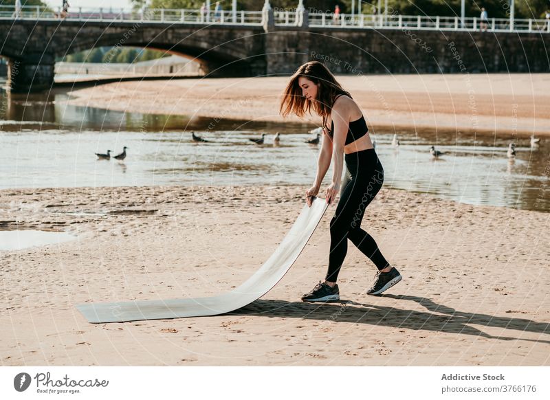 Woman preparing mat for yoga exercises woman prepare beach summer river slim peaceful female healthy fit body sportswear wellness tranquil sand harmony physical