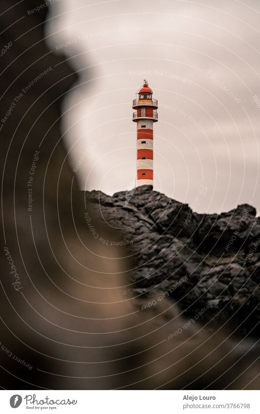 Red and white lighthouse seen behind vulcanic rocks on a grey day. beacon building canary coast coastline europe gran canaria island landmark landscape maritime