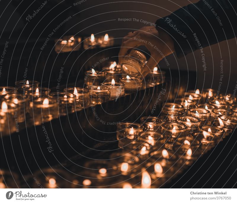 Candle altar in a church. Female hand lighting a candle. Sea of lights. shoulder stand Religion and faith Belief Love Hope Grief commemoration Prayer Church