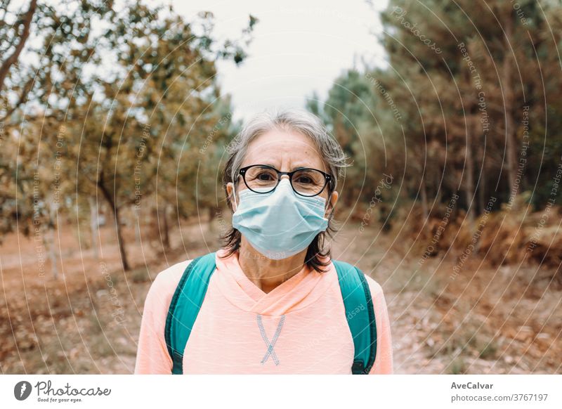 Close up of a frontal portrait of an old woman wearing a mask and sport clothes in the forest during a trekking day person elderly exercising fear horizontal