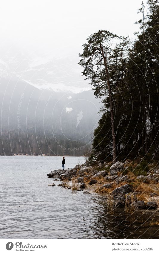 Lonely traveler near lake in mountainous terrain winter highland lonely admire vacation scenery explorer germany austria pond shore landscape rocky coast cold