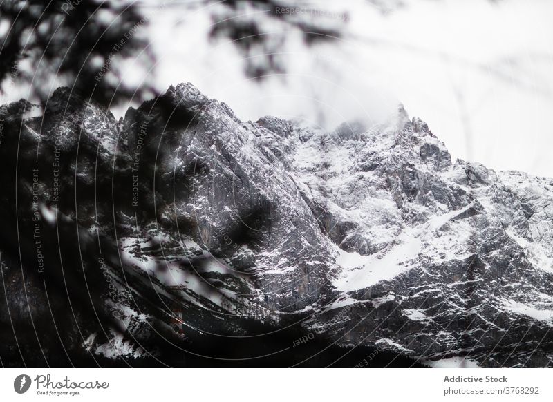 Rough rocky mountain slope covered with snow and forest rough ridge cold overcast gloomy majestic nature landscape gray autumn weather season range environment