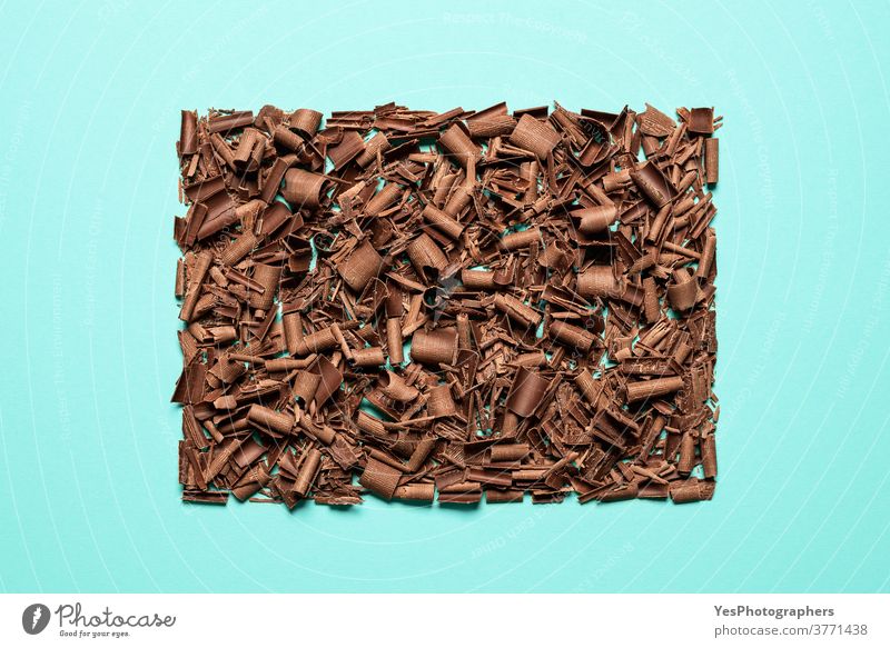 Chocolate pieces pile isolated on blue background. Chopped chocolate top view baking bitter brown chocolate shavings chopped christmas chunks confectionery