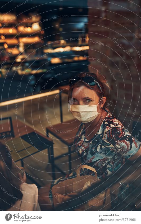 Young woman sitting in coffee shop at store front in the city center, wearing the face mask to avoid virus infection caucasian conversation covid-19 lifestyle