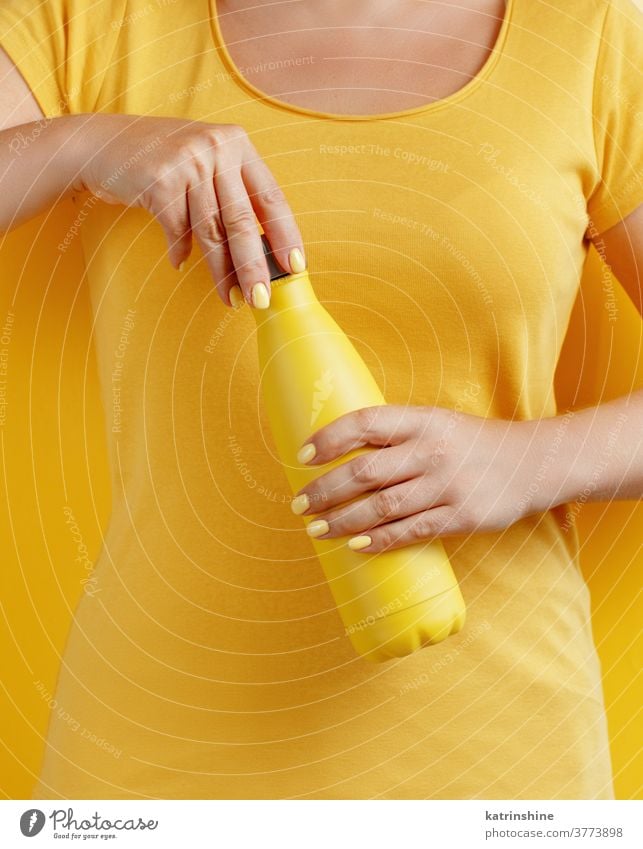 Close up of woman holding yellow reusable bottle on yellow background hand monochrome ecologic water steel thermo open bright mockup faceless aluminum blank