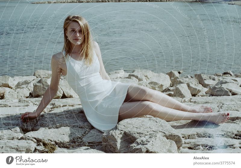 Backlit portrait of a young, barefoot woman on the banks of the Rhine, sitting on a stone dam Woman Young woman Slim already athletic Blonde youthful red blonde