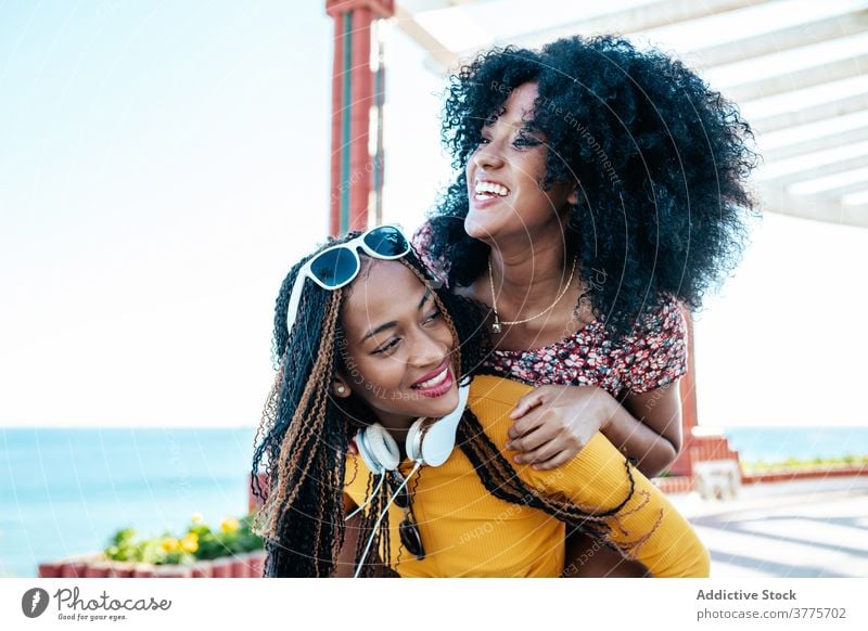 Black female friends having fun on embankment in summer piggyback women delight weekend best friend promenade ethnic black african american braid curly hair