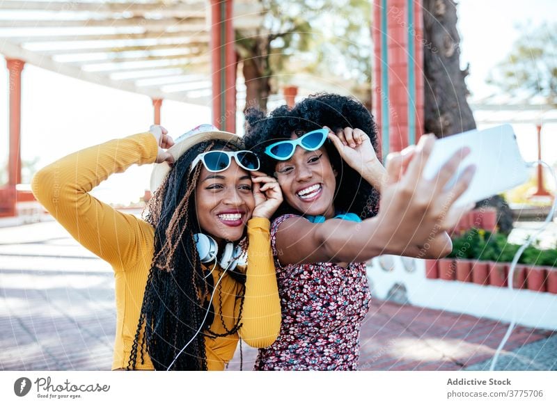 Cheerful black friends taking selfie in city hug smartphone women friendship cheerful bonding using summer promenade ethnic african american braid curly hair