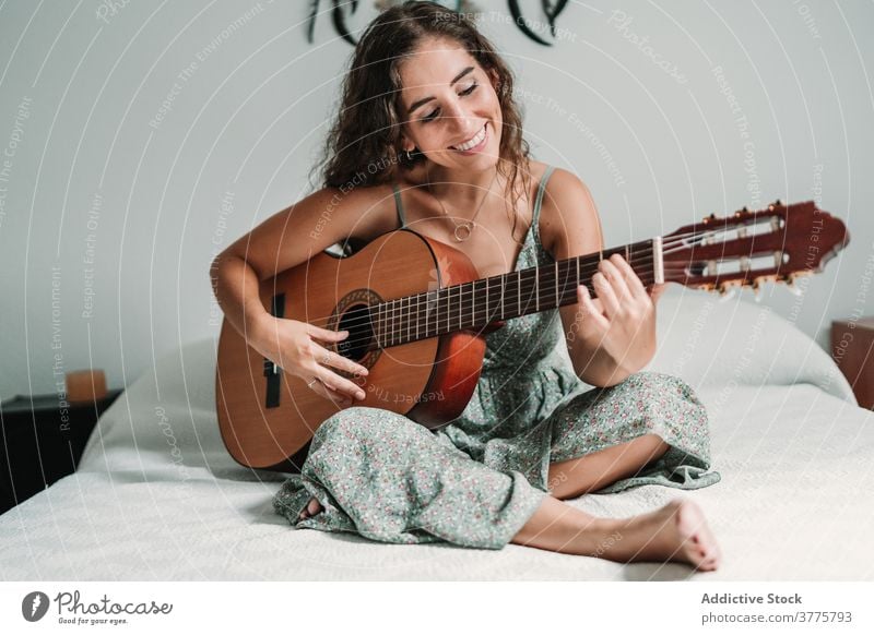 Positive woman playing guitar in bedroom guitarist music cheerful laugh talent entertain carefree instrument female ethnic acoustic cozy home happy musician