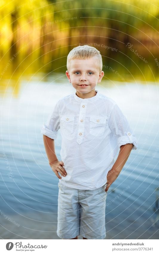 Portrait of a happy and beautiful little boy with blond hair and a white shirt, Happy childhood. Positive emotion. portrait near the river in nature yellow