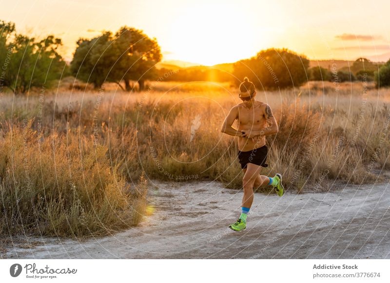 Energetic man running on sandy road runner wristwatch check sportsman athlete cardio move male rural strong body fitness active healthy energy exercise intense