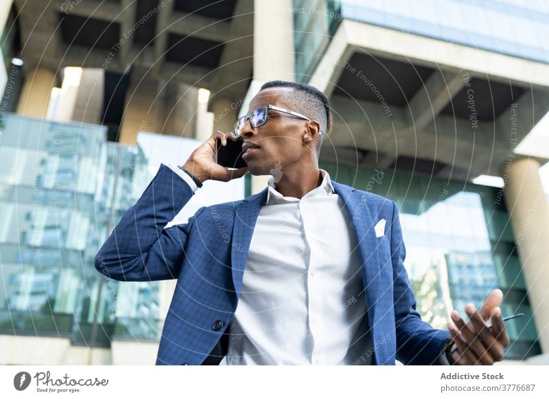 Serious businessman speaking on smartphone in downtown entrepreneur office building discuss suit determine using talk male ethnic black african american glass