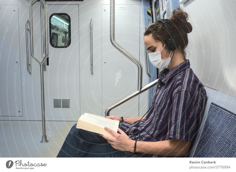 Concentrated masked millennial reading a book and listening to music in subway metro underground headphone sitting man young student teenager university college