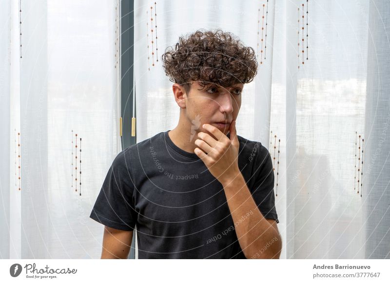 Attractive young man with curly hair wearing black t-shirt posing on white curtains background cheerful casual smile male adult handsome happy attractive