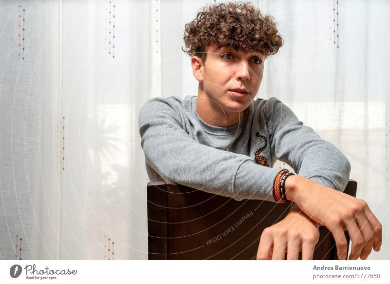 Attractive young man with curly hair wearing gray sweatshirt posing on white curtains background cheerful casual smile male adult handsome happy attractive