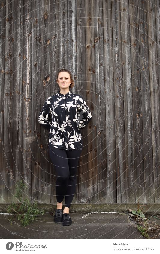 Young woman leans against a board wall and looks into the camera Expectation Colour photo Looking into the camera Uniqueness Summer Exterior shot Self-confident