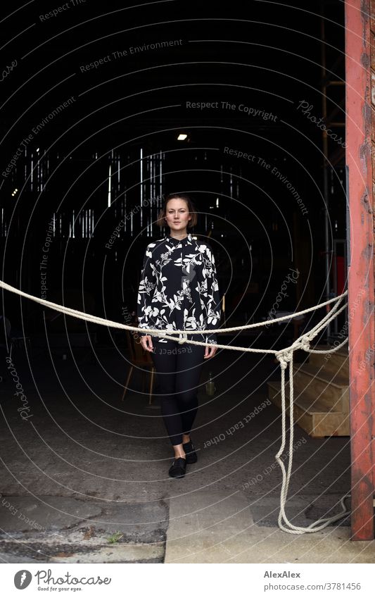 Young woman stands in a gate entrance behind a rope Expectation Colour photo Looking into the camera Uniqueness Summer Exterior shot Self-confident Athletic