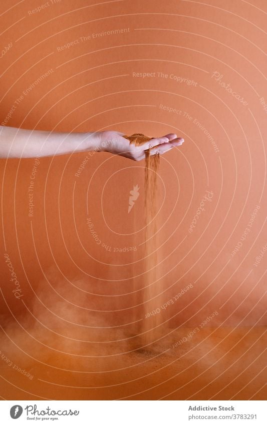 Crop person with sand in studio handful through finger pour natural soil dry sensual gentle tender dust dusty cloud inspiration creative art peaceful delicate