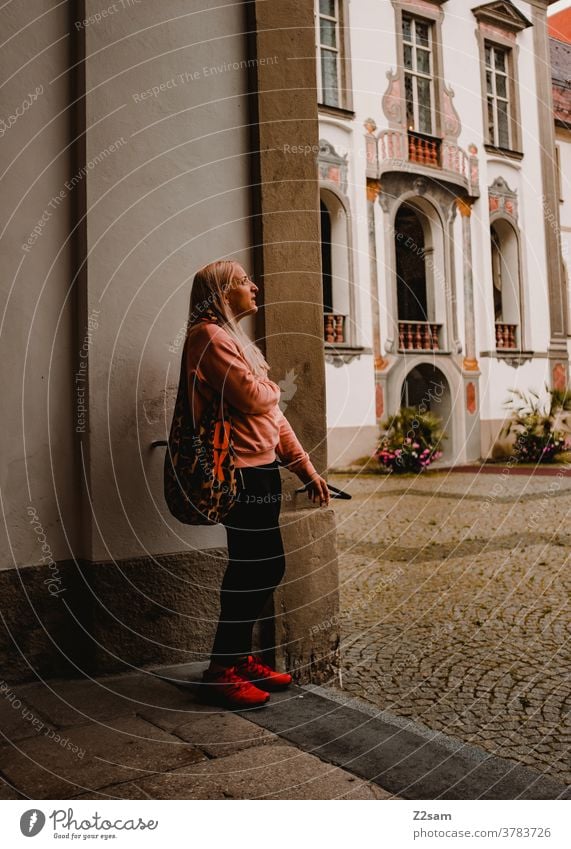 Young woman stands in front of the castle Füssen Sightseeing feet Bavaria Athletic back view Blonde long hairs fashionable traditon Lock Entrance Museum Culture