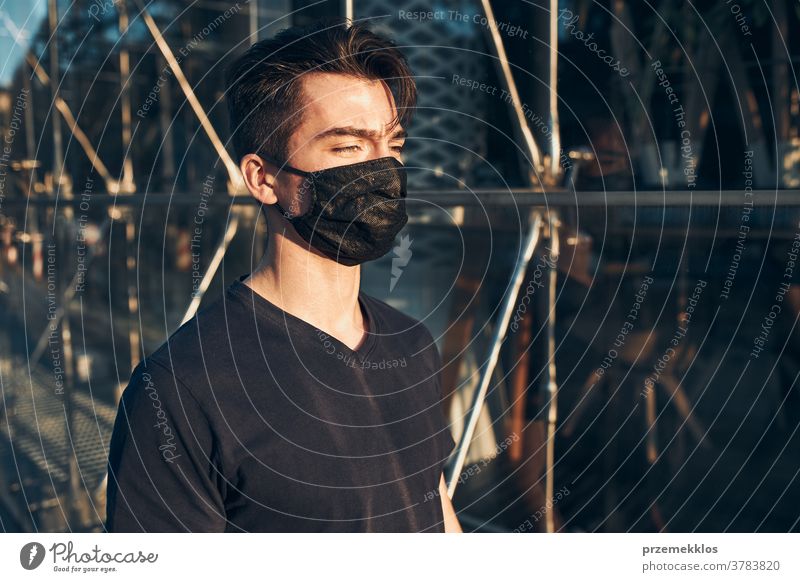 Young man walking in the city center along glass store front wearing the face mask to avoid virus infection boy care caucasian contagious conversation corona