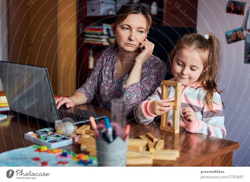 Woman mother working doing her job remotely during video chat call stream online course webinar on laptop from home while her daughter playing with bricks toy