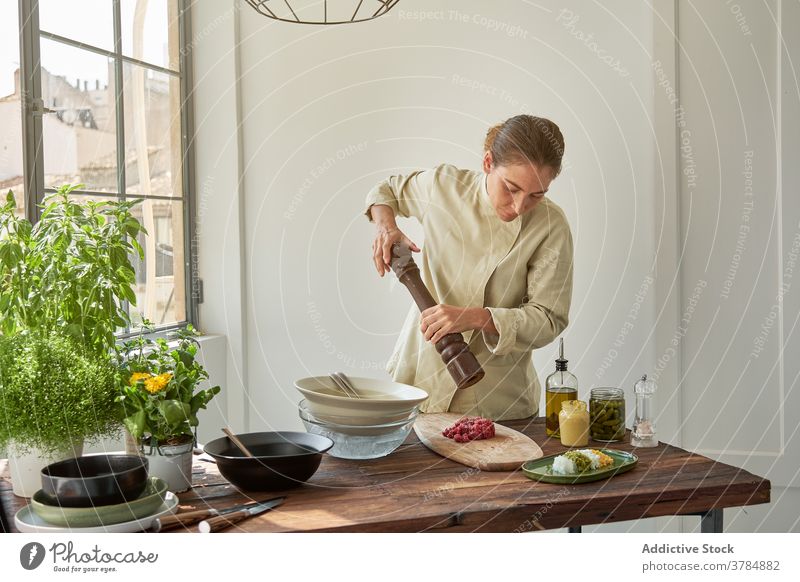 Woman cooking Steak tartare at home pepper mill seasoning add woman steak tartare raw meat beef female uniform chef serious food prepare kitchen cuisine meal