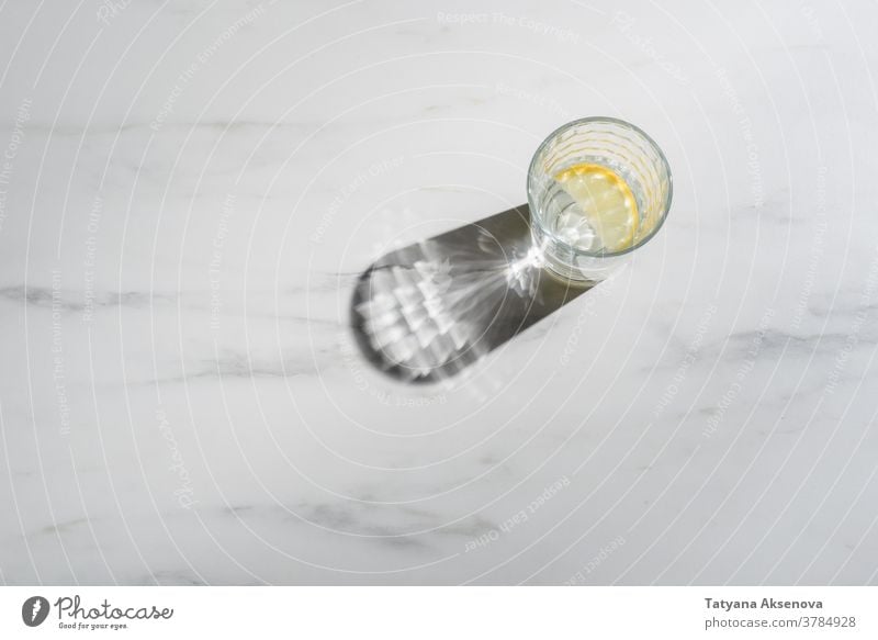 Glass of water with lemon pieces on marble background. Immune boosting morning drink fresh fruit glass cold citrus beverage