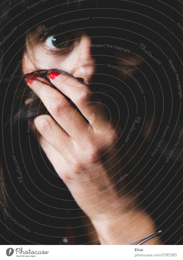 Woman looks panic-stricken with fear into the camera and holds her hand in front of her mouth. Panic Shock Fear Concern hand in front of mouth misfortune