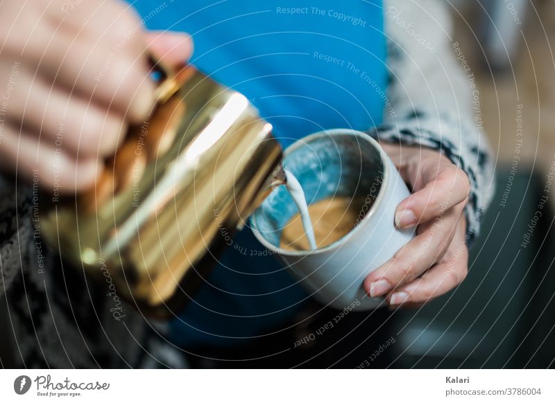 Woman in blue pouring latte art with milk foam into glass of latte in hand with copper pot Café au lait Cast barista latte type café au lait Espresso