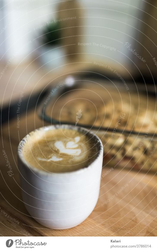 A mug of latte coffee with latte art flower on a wooden table with a crumble in a baking dish latte type Coffee Cappuccino Flower served Cake Coffee break