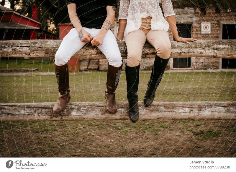 Latino man and woman sitting on two posts legs latino free air field patagonia spring riding day white brown pants hands background trees green