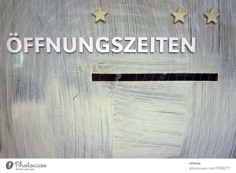 The white lettering "ÖFFNUNGSZEITEN" and three golden stars are left - otherwise the white paint prevents the view through the glass pane opening hours Stars