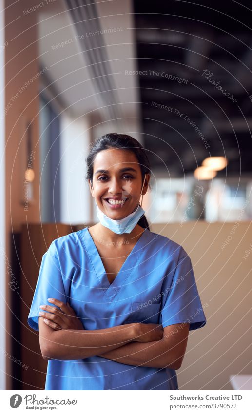 Smiling Female Doctor With Face Mask Wearing Scrubs In Busy Hospital During Health Pandemic doctor nurse scrubs key worker female woman wearing face mask