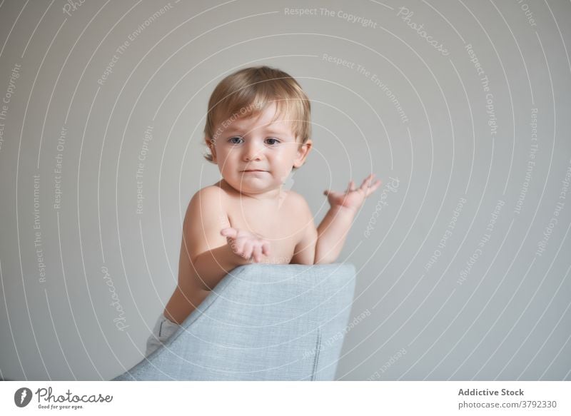 Cute boy standing in armchair at home clap hand cheerful adorable child little toy kid positive cute fun joy having fun childhood innocent happy glad