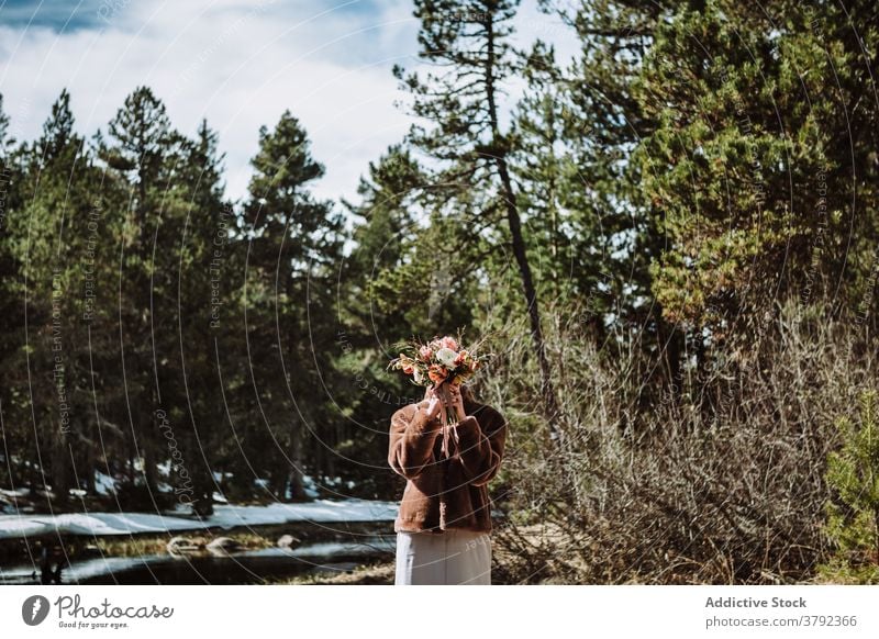 Unrecognizable woman holding bouquet against face in spring forest hide cover face flower nature disguise bloom warm clothes romantic tranquil calm sunny