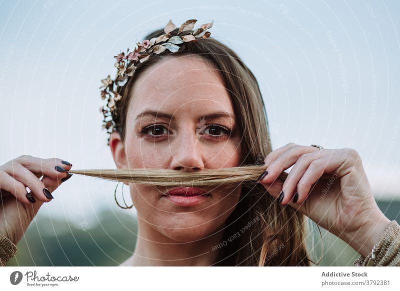 Attractive woman holding hair strand under nose calm gesture charming appearance cool positive having fun look wreath peaceful tranquil style attractive young