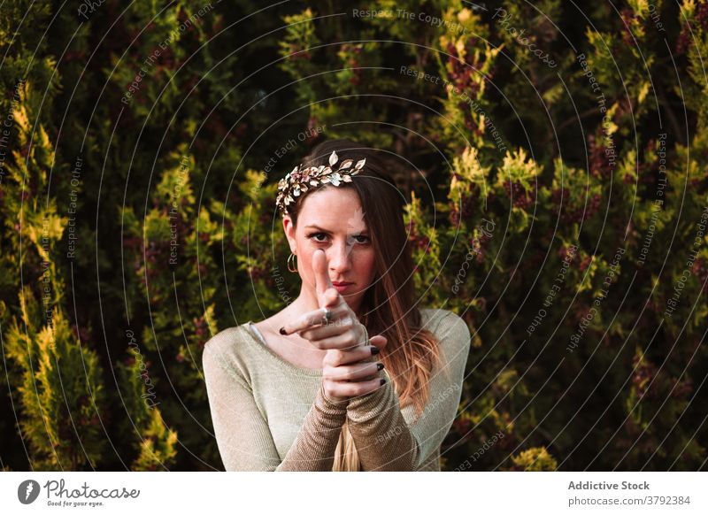 Serious woman in headband pointing finger gun at camera confident gesture serious style symbol threat shoot accessory calm individuality pistol demonstrate