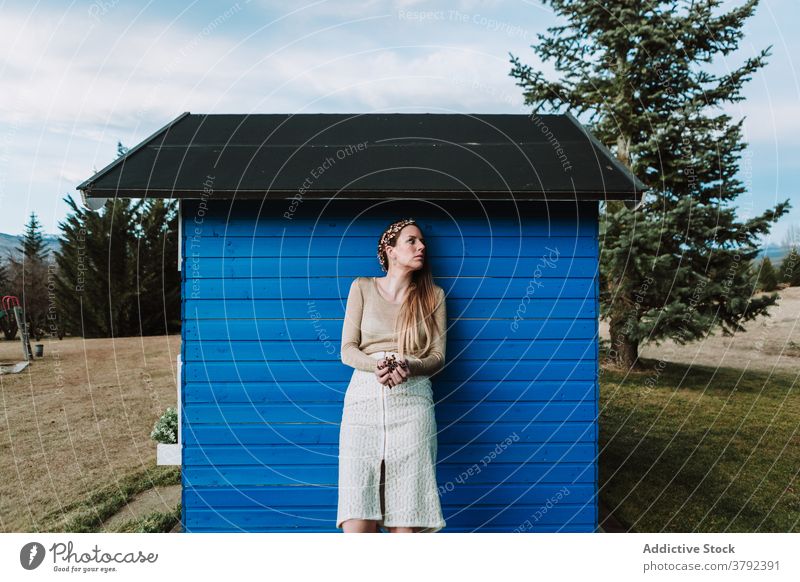 Unemotional woman in headband leaning on rural wooden structure positive style lean on elegant construction countryside gentle unemotional trendy nature