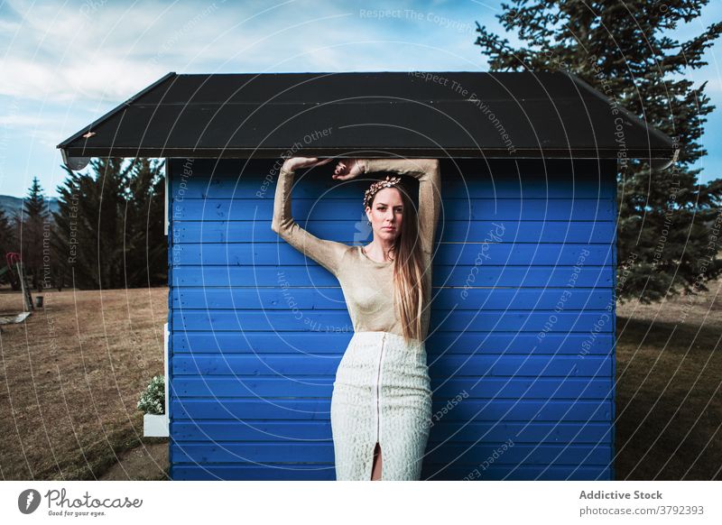 Unemotional woman in headband leaning on rural wooden structure positive style lean on elegant construction countryside gentle unemotional trendy nature