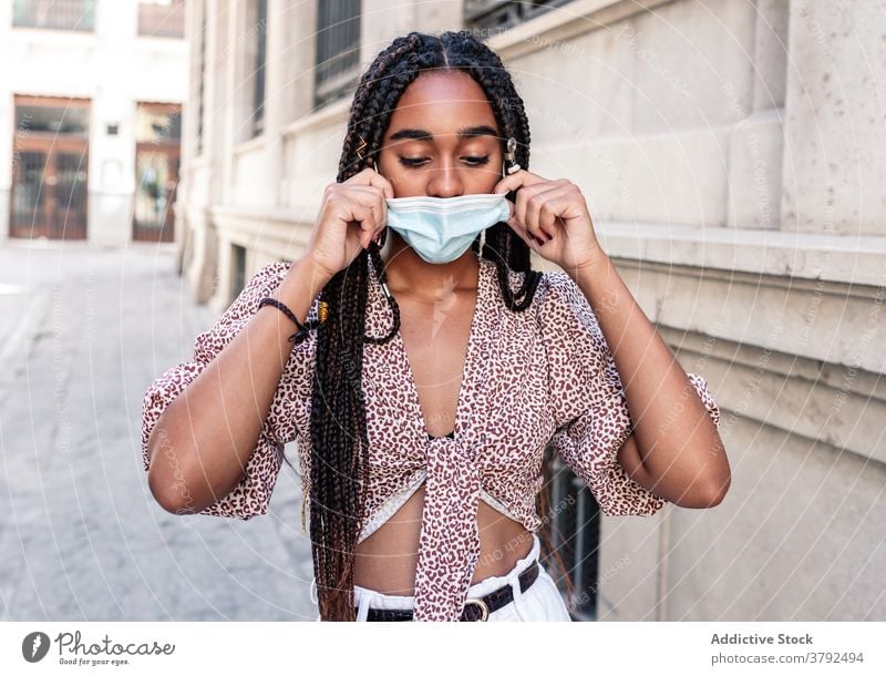 Stylish ethnic woman in medical mask on street style put on adjust city outbreak covid 19 female black african american braid hairstyle outfit trendy urban