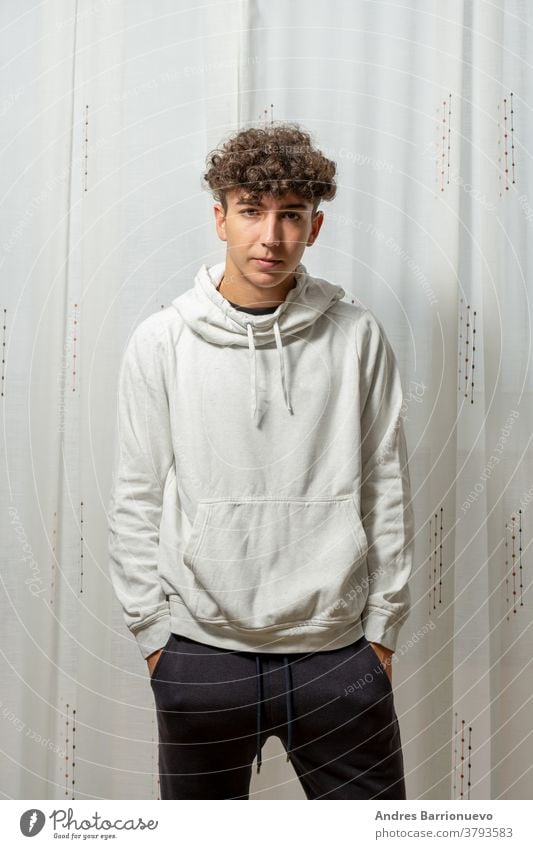 Attractive young man with curly hair wearing white sweatshirt posing on white curtains background cheerful casual smile male adult handsome happy attractive