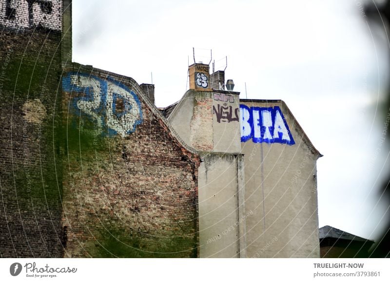 Gloomy Berlin fire walls from wartime in Prenzlauer Berg, partly plastered, with graffiti on top - how did they do it - and three or four chimneys in front of a light grey sky