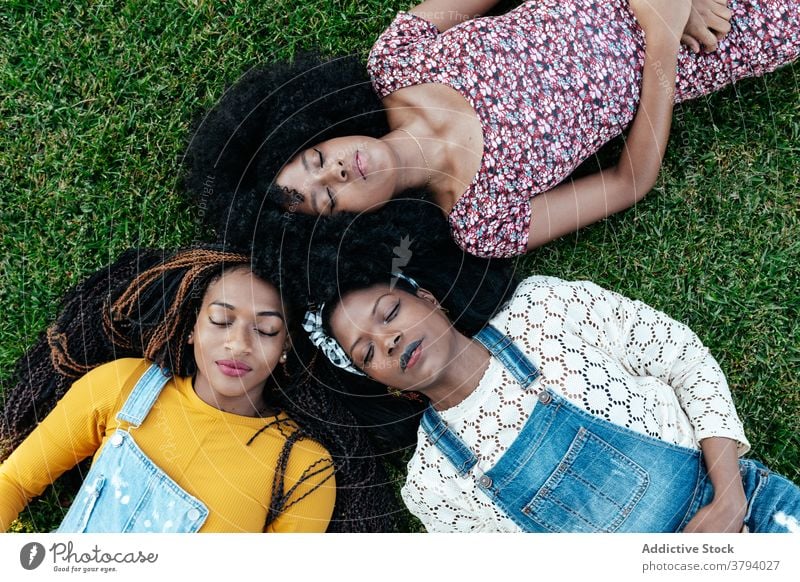 Diverse women lying on grass in park friendship positive together friendly bonding young multiethnic multiracial diverse black african american green lawn