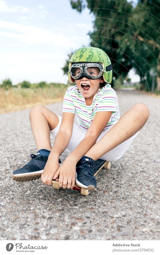 Happy boy on skateboard in protective eyeglasses helmet goggles having fun carefree childhood excited content road stylish apparel decorative summer trendy