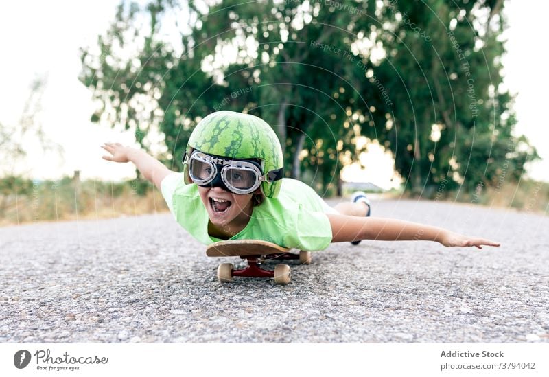 Positive kid on skateboard in safety glasses and decorative helmet boy having fun carefree enjoy mouth opened activity road goggles childhood excited content